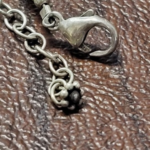 K&ouml;nnte beinhalten: Nahaufnahme eines silbernen Kettenarmbands mit einem Karabinerverschluss und einer dekorativen Perle. Die Perle ist silberfarben mit einem schwarzen Zentrum.