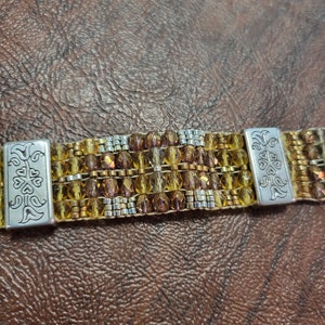 May include: A multi-strand beaded bracelet with gold and silver beads. The bracelet has two silver clasps with a floral design.