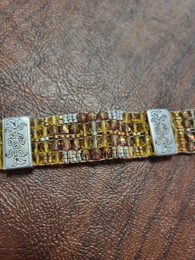 May include: A multi-strand beaded bracelet with gold and silver beads. The bracelet has two silver clasps with a floral design.