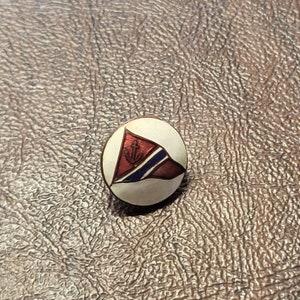 May include: A white enamel pin with a red, white, and blue flag with an anchor in the center.