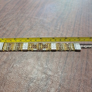 May include: A silver and gold beaded bracelet with a heart charm. The bracelet measures approximately 8 inches in length.