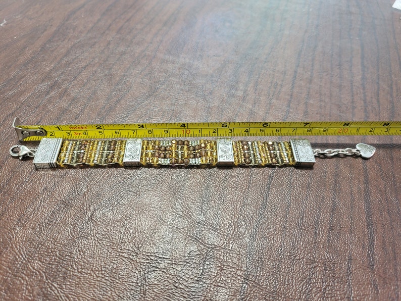 May include: A silver and gold beaded bracelet with a heart charm. The bracelet measures approximately 8 inches in length.