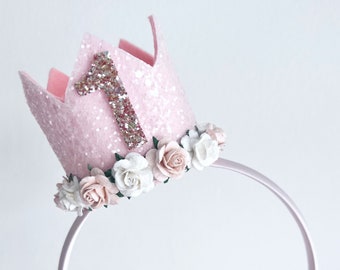 Op de afbeelding: Roze vilt kroon haarband met een glitterend nummer één en een bloemige rand. De haarband is gemaakt van dun, flexibel plastic.