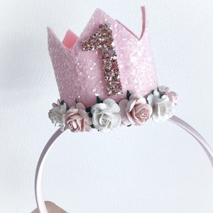 May include: Pink felt crown headband with a glittery number one and a row of white and pink flowers around the base.