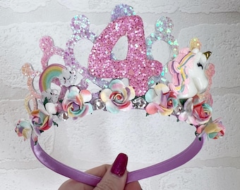 May include: A pink glittery headband with a number four, a rainbow, and a unicorn. The headband is decorated with pastel flowers and rhinestones.