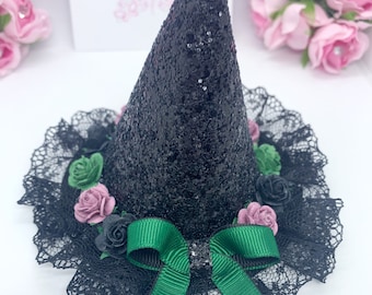 Puede incluir: Un sombrero de bruja negro con flores verdes y rosas, un lazo verde y un borde de encaje negro.