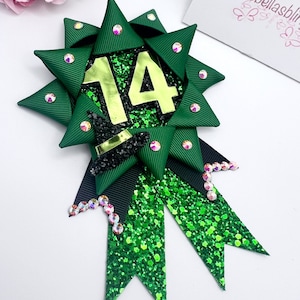 May include: Green and black glitter bow with a witch hat and the number 14 in gold glitter. The bow is decorated with iridescent rhinestones.
