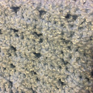 May include: Close-up of a light blue crocheted fabric with a shimmery sheen. The fabric is made with a soft, fluffy yarn.