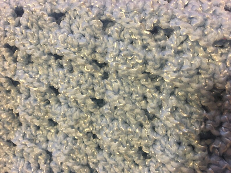 May include: Close-up of a light blue crocheted fabric with a shimmery sheen. The fabric is made with a soft, fluffy yarn.