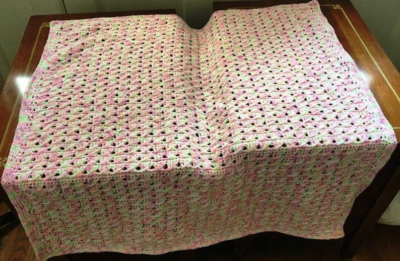 May include: A crocheted baby blanket in pink, white and green. The blanket is made with a delicate stitch pattern and has a soft, fluffy texture.