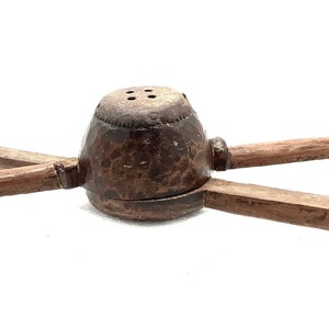 Könnte beinhalten: Ein Holz-Zitronenpresse mit zwei Griffen. Die Presse ist aus dunkelbraunem Holz und hat eine runde, schalenförmige Oberseite mit vier Löchern.