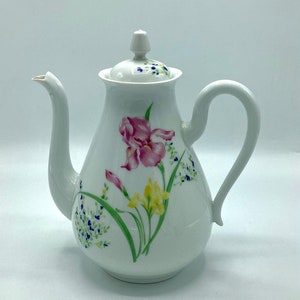 Könnte beinhalten: Weiße Porzellan-Teekanne mit floralem Design mit rosa, gelben und blauen Blumen. Die Teekanne hat einen Deckel mit einem Knopf oben.