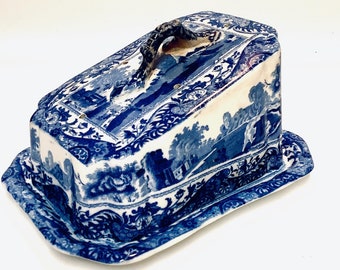 May include: A blue and white ceramic butter dish with a lid and a handle. The dish is decorated with a floral pattern and a landscape scene.