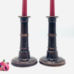 May include: Two dark brown wooden candle holders with a bamboo design. Each holder has a red candle.