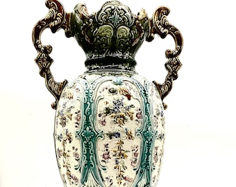 May include: A large, ornate, green and white ceramic vase with gold accents and floral designs. The vase has two handles and a wide base.