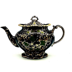 May include: A black teapot with gold and green floral designs. The teapot has a lid and a handle.