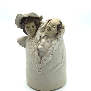 May include: A ceramic sculpture of a couple, a woman wearing a hat and a man with a beard, both with painted faces, standing close together.