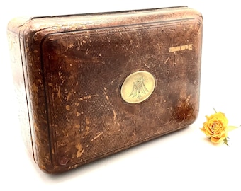 May include: A vintage, brown leather box with a brass monogram on the lid. The box has a worn, distressed look and is closed.