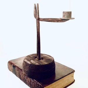 May include: A rustic metal candlestick with a wooden base. The candlestick is made of iron and has a simple design. The base is made of wood and is stained a dark brown colour.