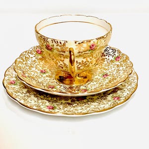 Könnte beinhalten: Ein Vintage-Teetassen- und Untertassen-Set mit einem zarten Blumenmuster und goldenen Akzenten. Tasse und Untertasse sind aus feinem Knochenporzellan gefertigt und haben eine cremefarbene Basis mit einem goldenen Blumendesign.