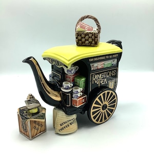 May include: A black and yellow Ringtons Tea teapot shaped like a vintage delivery wagon. The teapot has gold accents, a small basket on top, and miniature tea cups and boxes. The words "Ringtons Tea" and "Quality Teas" are visible.