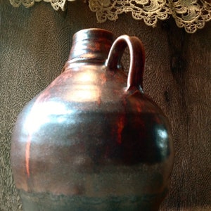 May include: A large, brown ceramic jug with a wide mouth and a handle. The jug has a glossy finish and a rustic appearance.