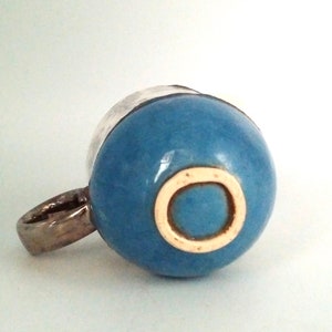 May include: A blue ceramic mug with a white rim and a white circle on the bottom. The mug has a silver handle.