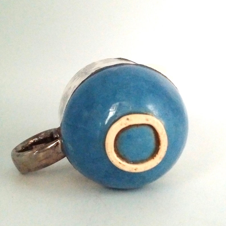 May include: A blue ceramic mug with a white rim and a white circle on the bottom. The mug has a silver handle.