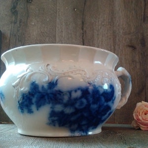 Op de afbeelding: Een witte keramische chamberpot met blauwe bloemenmotieven en een reliëf rond de rand.