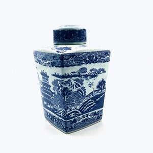 May include: A blue and white porcelain jar with a lid. The jar has a square shape and features a traditional Chinese landscape design with a pagoda, trees, and a river.