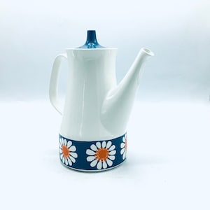 May include: White ceramic teapot with a blue lid and a band of orange and white daisy flowers around the bottom.