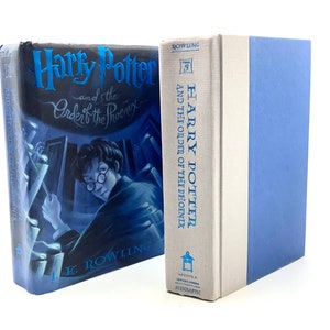 May include: A hardcover copy of Harry Potter and the Order of the Phoenix, book five in the Harry Potter series by J.K. Rowling. The book cover features a blue and white illustration of Harry Potter with glasses looking over his shoulder.