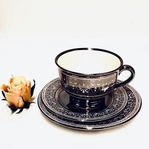 May include: A silver teacup and saucer set with intricate floral designs. The cup and saucer are both black with silver accents.
