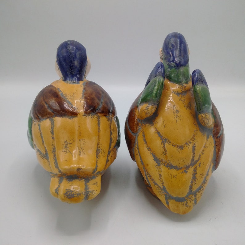Pu&ograve; includere: Due figurine in ceramica di uccelli con vernice marrone, gialla, verde e blu. Gli uccelli sono rivolti in direzioni opposte.