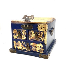 May include: A small blue wooden box with gold accents and three drawers. The box has a hinged lid and brass hardware.