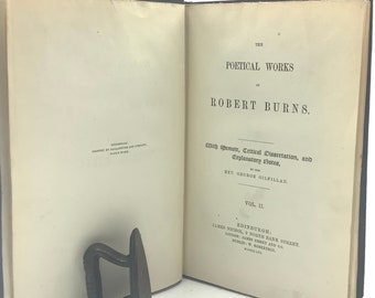 Pode incluir: Um livro antigo intitulado "The Poetical Works of Robert Burns" com uma designação de volume II. O livro está aberto em uma página com o título e o nome do autor. O livro é encadernado em preto e tem uma aparência desgastada e envelhecida.