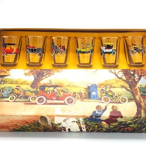 May include: Set of six vintage shot glasses with gold rims. Each glass features a different vintage car design in colorful detail. The glasses are displayed in a box with a colorful illustration of a country scene.