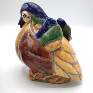 Pu&ograve; includere: Una statuetta di uccello in ceramica con una glassa blu, verde e marrone. L'uccello &egrave; appollaiato su una base e ha una superficie screpolata e testurizzata.