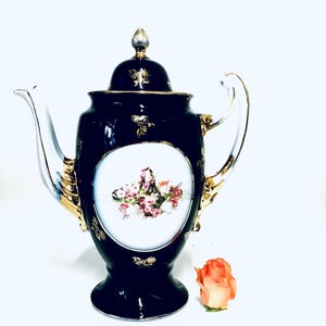 May include: A black and gold porcelain teapot with a floral design and a white background. The teapot has a lid and a handle.