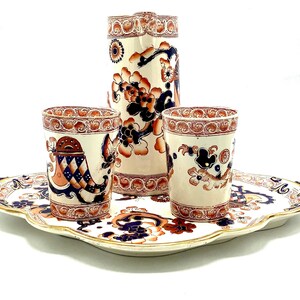 May include: A vintage blue and white porcelain tea set with a jug and two cups on a matching tray. The set features a floral pattern with red and gold accents.