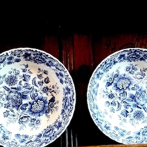 May include: Two white ceramic bowls with blue floral patterns. The bowls have a scalloped edge and are decorated with a repeating floral design.