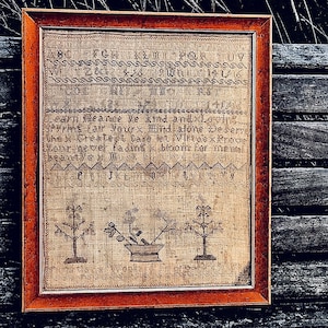 Könnte beinhalten: Ein antiker, gerahmter Stich mit braunem Leinenhintergrund und rotem Rahmen. Der Stich zeigt ein Kreuzstich-Design mit drei Bäumen und einem Blumentopf. Der Text auf dem Stich lautet "Learn Meance ye and andxLovin Sprins Fair Yourx hind stone Deserve the x Createst Care let. Virtue x Proone Your never fadins x bloom for mental".