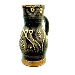 May include: A small, dark brown ceramic pitcher with a handle. The pitcher has a white and yellow geometric design.