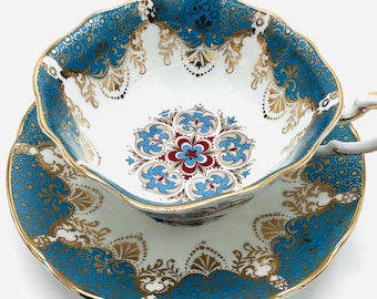 May include: A blue and gold teacup and saucer set with a floral design. The cup and saucer have a scalloped edge and are decorated with intricate gold details.