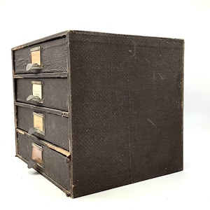 May include: A dark brown wooden drawer cabinet with five drawers. Each drawer has a metal pull handle and a small label.