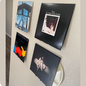 Puede incluir: Cuatro discos de vinilo expuestos en una pared blanca. Los discos se titulan "The Lumineers", "Foreigner", "Grass Roots" y "The Doors".