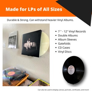 Puede incluir: Un juego de dos soportes de pared negros para discos de vinilo, dise&ntilde;ados para sostener discos de vinilo de 7 a 12 pulgadas. Los soportes se muestran sosteniendo un disco de vinilo amarillo y un disco de vinilo negro. El texto "Made for LPs of All Sizes" est&aacute; en la parte superior de la imagen. El texto "Durable & Strong. Can withstand heavier Vinyl Albums." est&aacute; debajo de la imagen. El texto "7" - 12" Vinyl Records", "Double Albums", "Album Sleeves", "Gatefolds", "CD Cases", y "Vinyl Discs" est&aacute; listado en el lado derecho de la imagen. El texto "Can also be used to display canvas, portraits, certificates, and more!" est&aacute; en la parte inferior de la imagen.