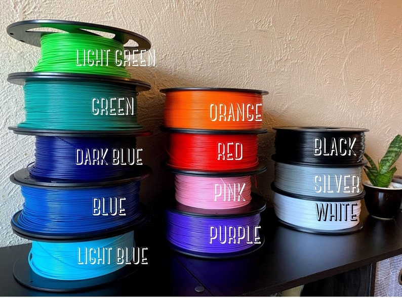 Puede incluir: Carretes de filamento en varios colores, incluyendo verde claro, verde, azul oscuro, azul, azul claro, naranja, rojo, rosa, morado, negro, plata y blanco. Los carretes est&aacute;n dispuestos en dos filas, con la fila superior que contiene los colores m&aacute;s claros y la fila inferior que contiene los colores m&aacute;s oscuros.