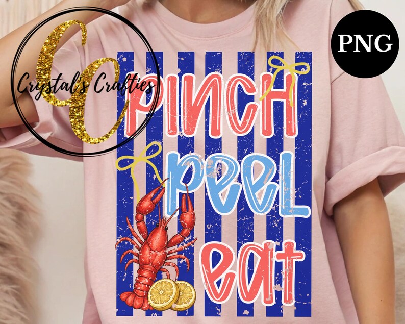 May include: Pink t-shirt with a graphic design featuring the words "Pinch Peel Eat" in red and blue, with a red crawfish and lemon slices. The design is set against blue and white vertical stripes.