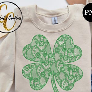 May include: A green four-leaf clover design with a lace pattern on a beige sweatshirt. The design is a digital graphic.